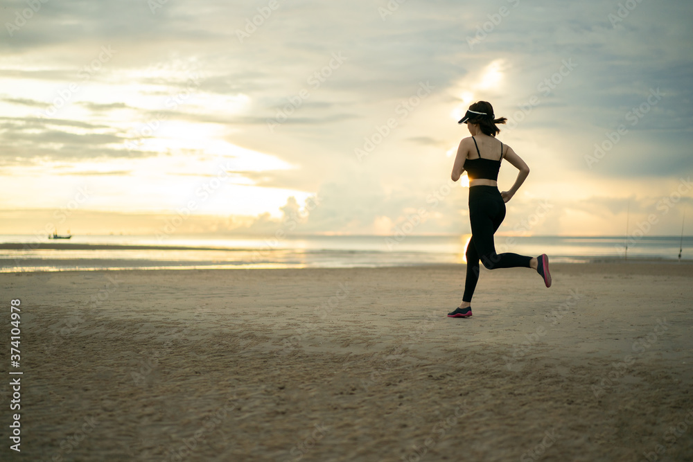 Side view of young woman in sportswear jogging on beach in the morning.