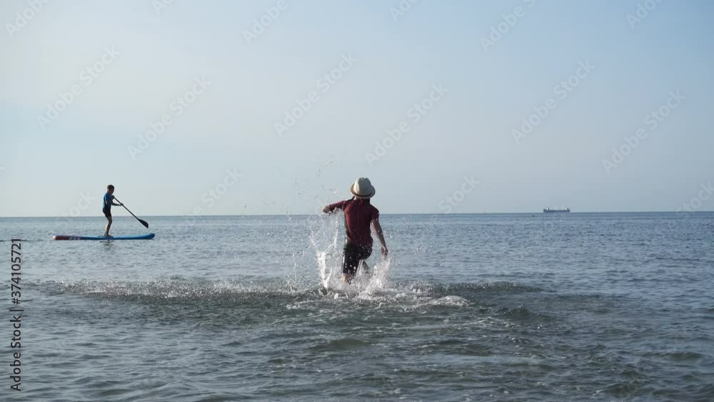 Happy siblings teen children in neoprene suits playing and paddling on sup board in Baltic sea Happy siblings teen children in neoprene suits playing and paddling on sup board in Baltic sea