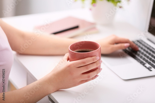 Woman drinking hot coffee in office, closeup