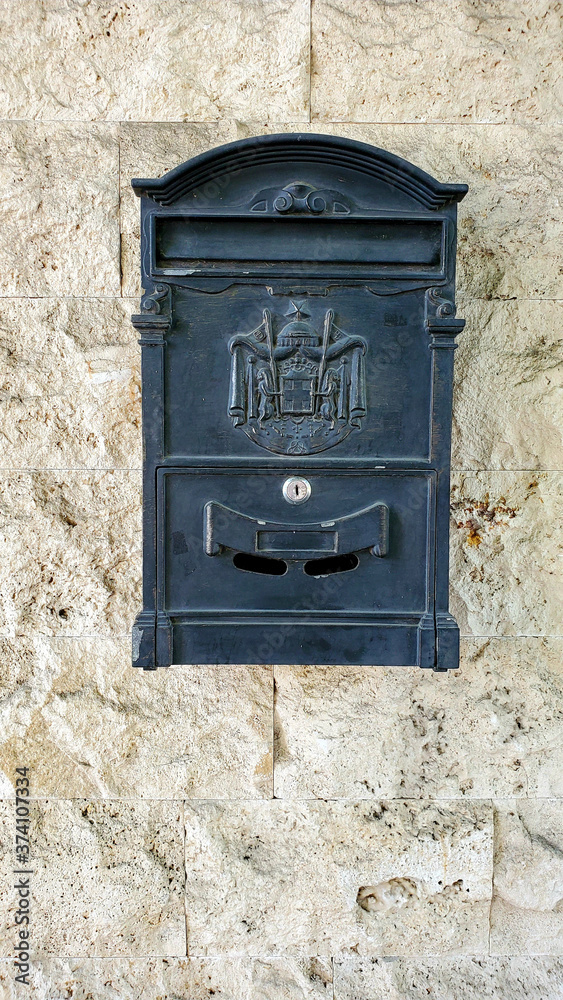 Old mailbox on the wall. Vintage mailbox with antique embossed emblem closeup on rough stone wall background with copy space
