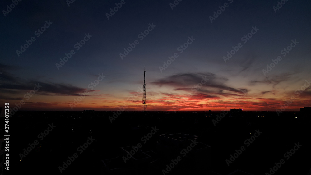 Sunset over the city. Night sundown over cityscape in darkness with industrial tower silhouette