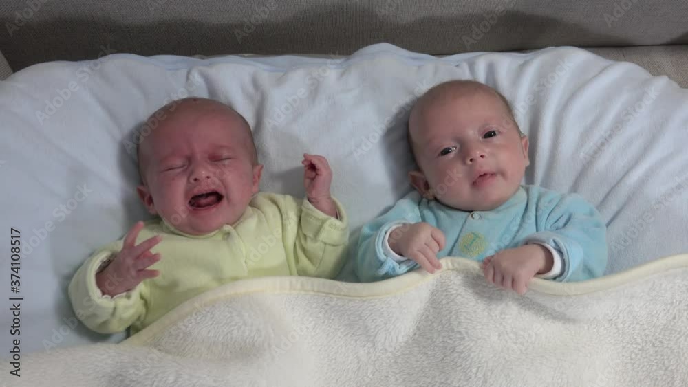 Two girls sisters lie on the bed. Two baby twins on the bed, one crying. Two girls sisters lie on the bed. Two baby twins on the bed, one crying.