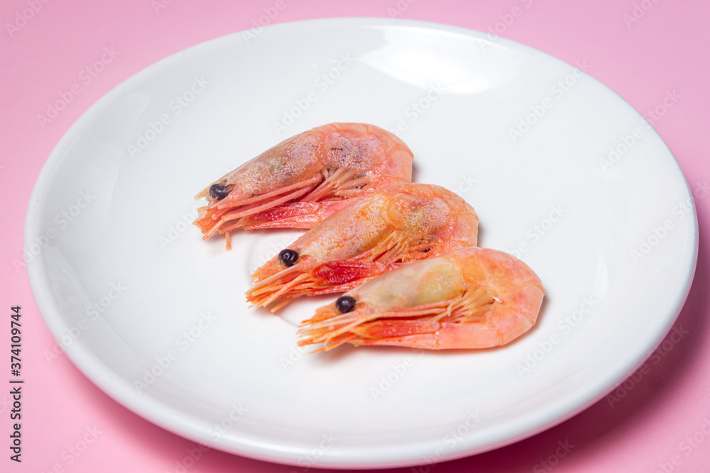 Shrimps on a white plate. Boiled shrimp in a plate on a pink background. Three shrimps lie next to each other Shrimps on a white plate. Boiled shrimp in a plate on a pink background. Three shrimps lie next to each other