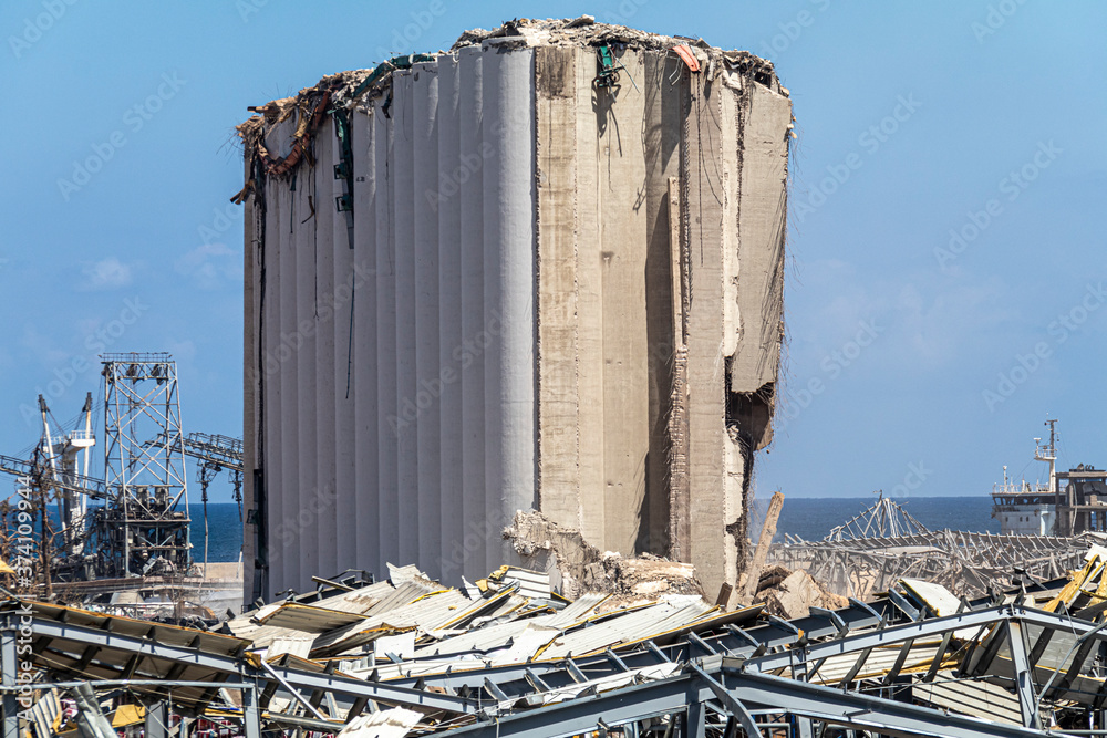 Fototapeta premium Skutki eksplozji w porcie w Bejrucie. Uszkodzony silos zbożowy, poskręcane metalowe konstrukcje i porozrzucane gruzy w trakcie trwających prac rekonstrukcyjnych.