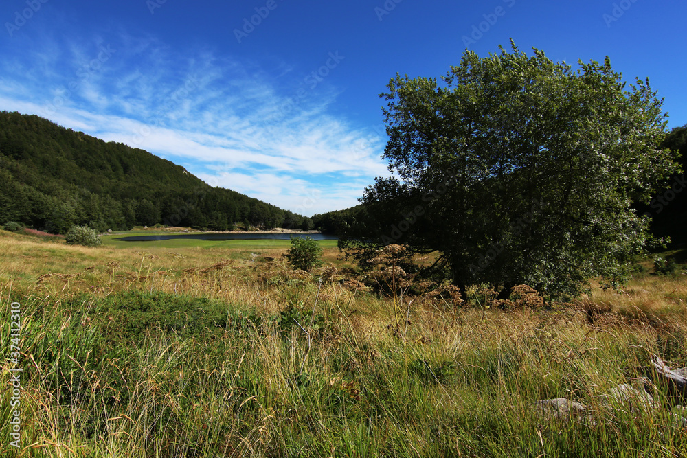Obraz premium Paesaggio estivo di montagna nell’Appennino modenese; veduta tra sentieri, boschi di faggio, rocce e un piccolo lago