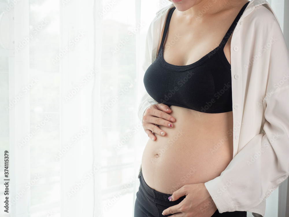 portrait of 4 months pregnant Asian woman in white bed room, Woman touching her abdomen belly on white background. portrait of 4 months pregnant Asian woman in white bed room, Woman touching her abdomen belly on white background.
