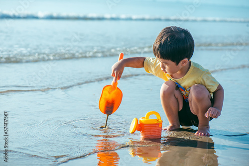 An Asian boy playing his orange toy at the beach in the morning.