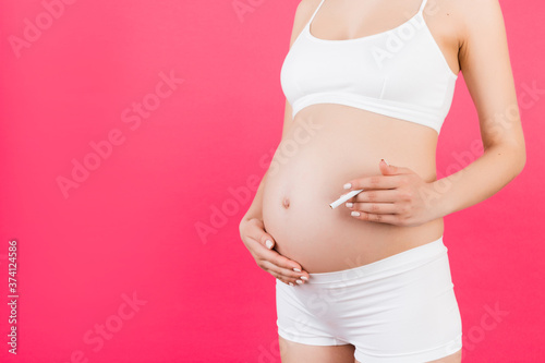 Close up of pregnant woman in white underwear with a cigarette against her belly at pink background. Dangerous risk for unborn baby © sosiukin