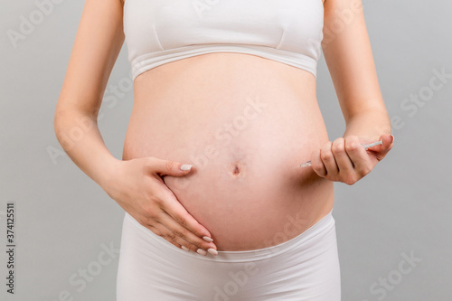 Cropped image of pregnant woman making insulin injection to control sugar level at colorful background with copy space. Healthcare concept