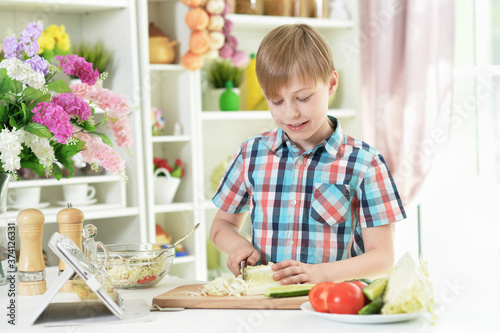 Boy preparing delicious fresh salad in kitchen