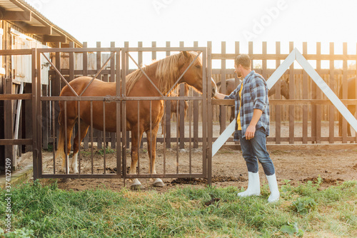 rancher in rubber boots and plaid shirt touching head of brown horse in corral