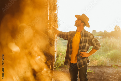 Obraz na płótnie selective focus of farmer in straw hat and plaid shirt touching bale of hay in s