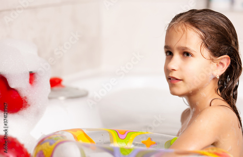 Funny little girl bathes in a bathtub with an inflatable lifebuoy