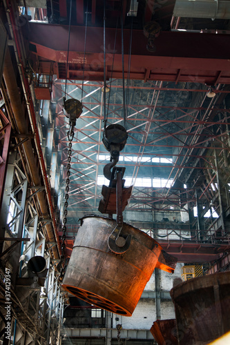 Metallurgy plant interior. Melting of metal. Metallurgy bucket with liquid hot metal. Orange light of furnace. photo