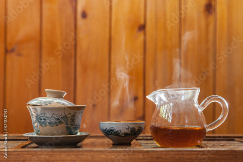 Chinese tea cup and glass kettle with cloud of vapor on wooden background