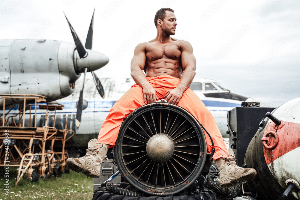 Naklejka premium Bodybuilder with large biceps sitting on airplane's turbine