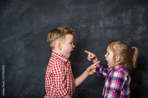 Boy and girl pointing fingers to each other. Raging kids - children shouting to each other against blackboard background. Angry kids