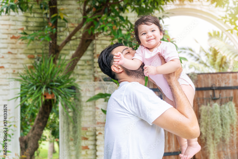 Cheerful father holding and kiss baby daughter in his hand while relax time at home. Mixed race little lovely girl with daddy carrying in the garden . Happy father day concept. Cheerful father holding and kiss baby daughter in his hand while relax time at home. Mixed race little lovely girl with daddy carrying in the garden . Happy father day concept.