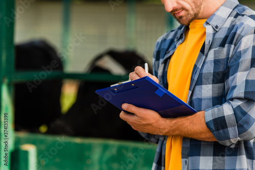 cropped view of farmer in plaid shirt writing on clipboard