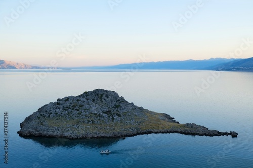 Boat sailing on the sea next to rocky island at dawn, Sveti Juraj, Croatia 