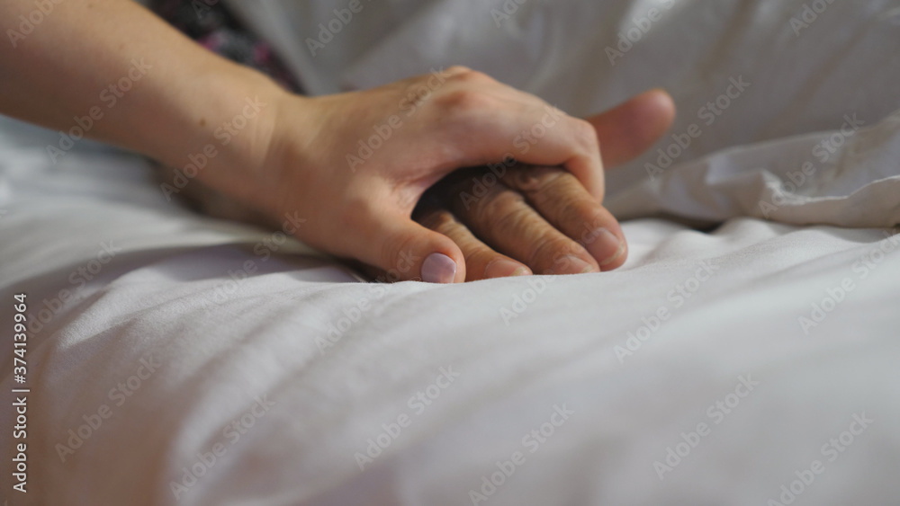 Girl takes and comforts hand of sick mature woman in medical clinic. Granddaughter gently touches wrinkled arm of her elderly grandmother lying in bed hospital. Daughter gives support to her parent