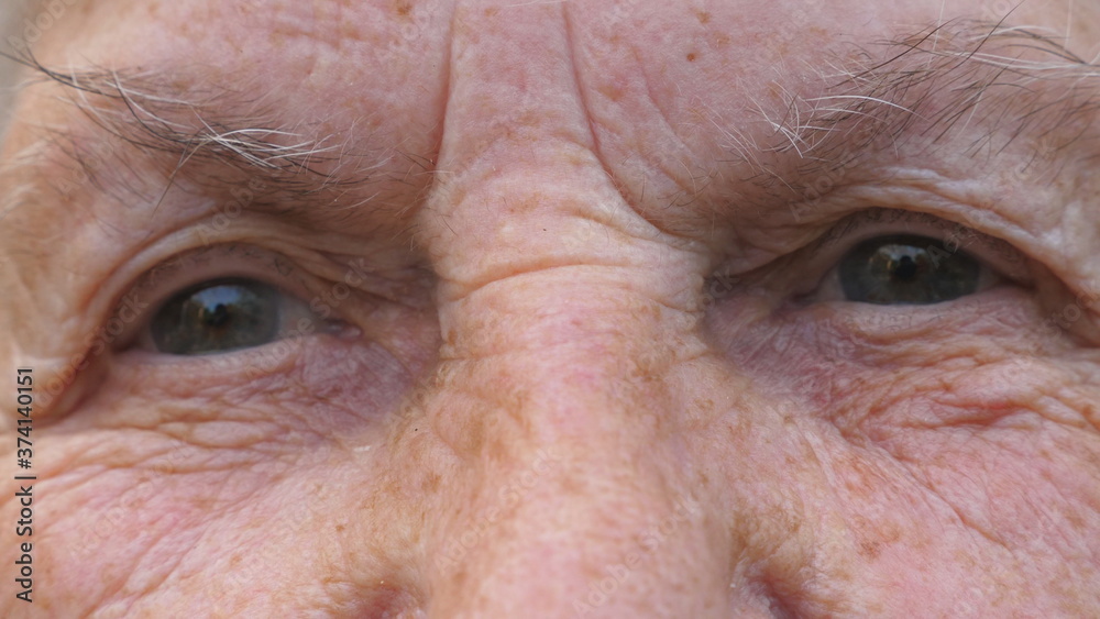 Portrait of elderly grandmother looks into camera with a sad sight. Close up gray eyes of mature woman with wrinkles around them. Sorrowful facial expression of senior grandma Portrait of elderly grandmother looks into camera with a sad sight. Close up gray eyes of mature woman with wrinkles around them. Sorrowful facial expression of senior grandma