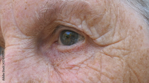 Portrait of half wrinkled female face looks into distance. Close up gray eye of mature woman stares and blinks with a disappointment sight. Facial expression of desperate and unhappy grandmother