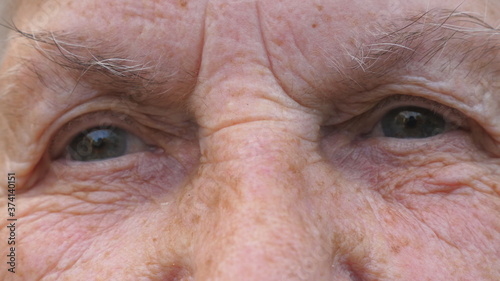 Portrait of elderly grandmother looks into camera with a sad sight. Close up gray eyes of mature woman with wrinkles around them. Sorrowful facial expression of senior grandma