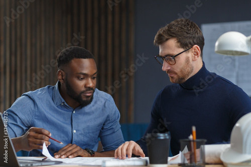 Multiracial engineer team working in office with blue prints and architect equipment sketching,discussing and planning construction project. Partners disputing at work. Business construction concept.