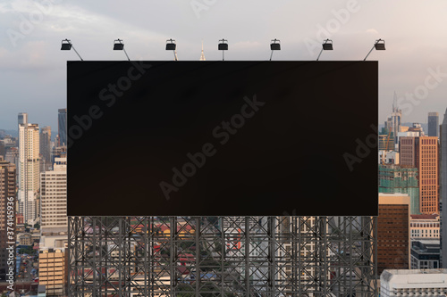 Blank black road billboard with Kuala Lumpur cityscape background at sunset. Street advertising poster, mock up, 3D rendering. Front view. The concept of marketing communication to promote or sell