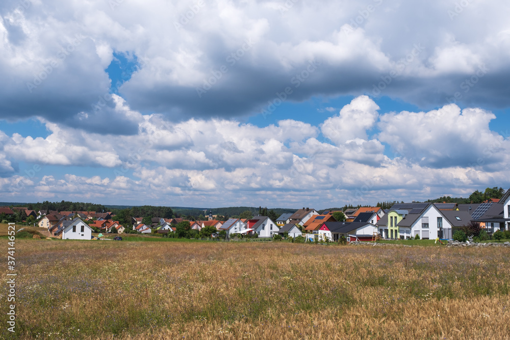 View across a field to a small village in Franconian Switzerland / Germany under a blue sky with white clouds View across a field to a small village in Franconian Switzerland / Germany under a blue sky with white clouds