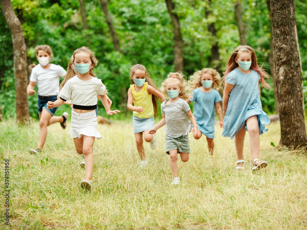Happy little kids wearing protective face mask jumping and running on meadow, forest. Looks happy, cheerful, sincere. Copyspace. Childhood, pandemic concept. Healthcare, coronavirus pandemic. Happy little kids wearing protective face mask jumping and running on meadow, forest. Looks happy, cheerful, sincere. Copyspace. Childhood, pandemic concept. Healthcare, coronavirus pandemic.