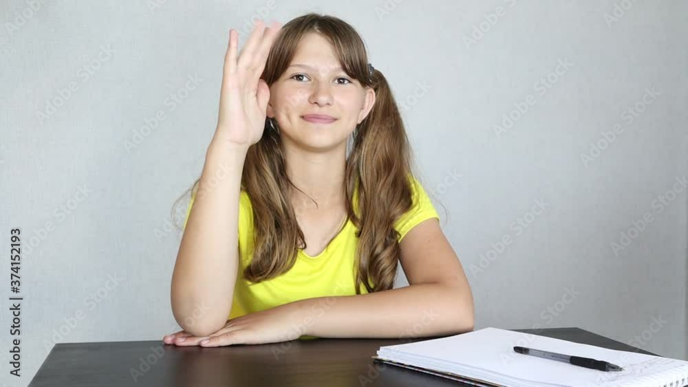 Schoolgirl raises her hand in class at the lesson. New school year, studying at home, doing homework Schoolgirl raises her hand in class at the lesson. New school year, studying at home, doing homework