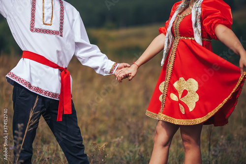 Dancing guy and girl dressed in national Russian clothes are holding hands Art grain and noise on photo