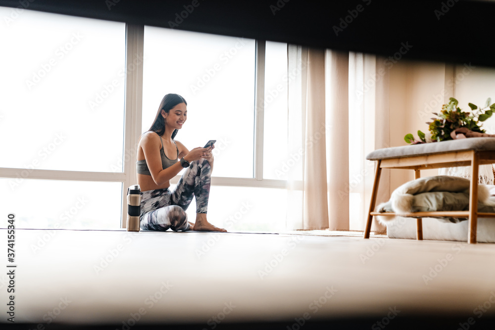Image of focused asian woman using cellphone while working out Image of focused asian woman using cellphone while working out