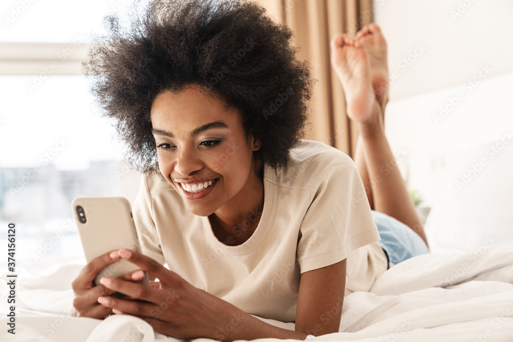 Image of cheerful african american girl smiling while using mobile phone Image of cheerful african american girl smiling while using mobile phone