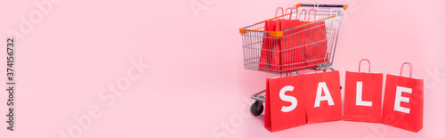 Foto Panoramic concept of word sale on red shopping bags near cart on pink surface
