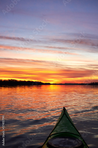 View from bow (prow) of green kayak at colorful sunset over Danube river at autumn time