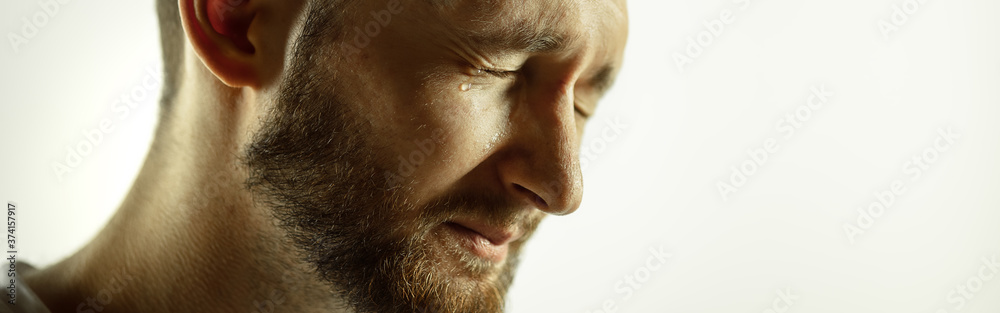 Obraz premium Crying. Caucasian young man's close up cropped shot on studio background, flyer. Concept of human emotions, facial expression, sales, ad. Copyspace. Beautiful male model with bright expression.