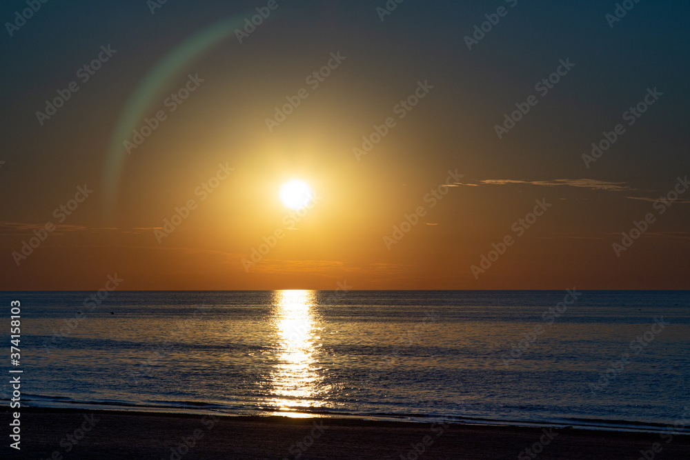 Beautiful sunset at the sea. Young people walk along the beach. People are watching the sunset. Sea and red-yellow sky. Silhouettes of people on the background of the sunset. In the evening by the sea Beautiful sunset at the sea. Young people walk along the beach. People are watching the sunset. Sea and red-yellow sky. Silhouettes of people on the background of the sunset. In the evening by the sea