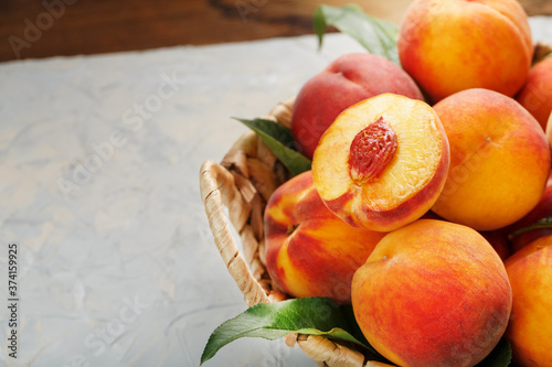 Peaches in a wicker basket on a stone gray table with a juicy peach slice with a stone pit. Top view, free space
