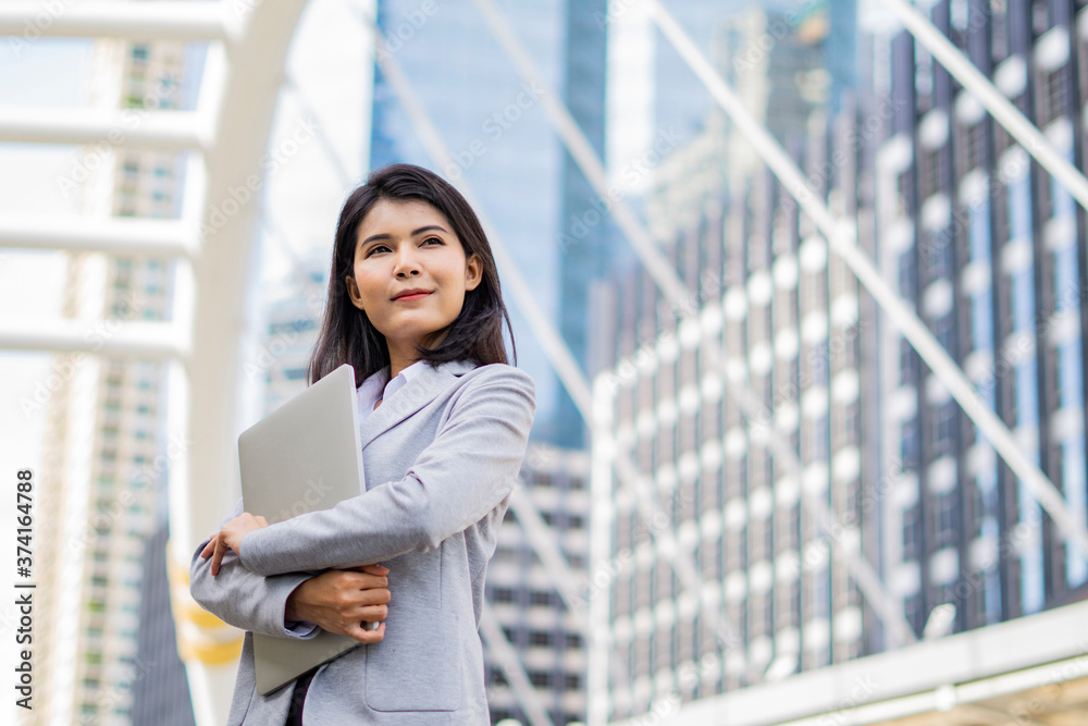 Business woman hold a laptop while standing on the property business background. Business woman hold a laptop while standing on the property business background.
