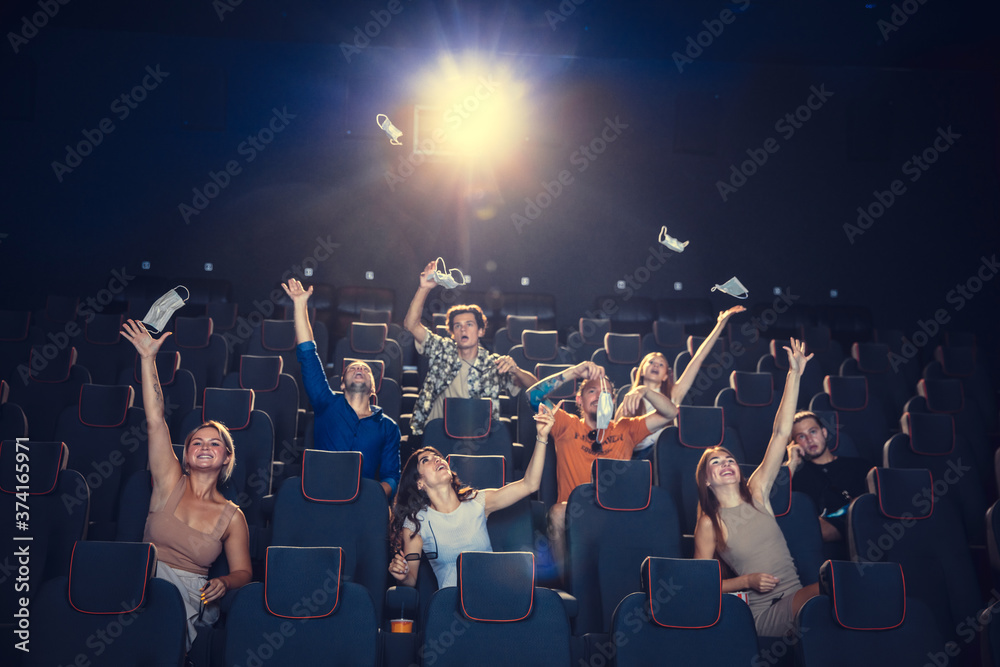 Cinema, movie theatre during quarantine. Coronavirus pandemic safety rules, social distance during movie watching. Men and women wearing protective face mask sitting in a rows of auditorium, eating
