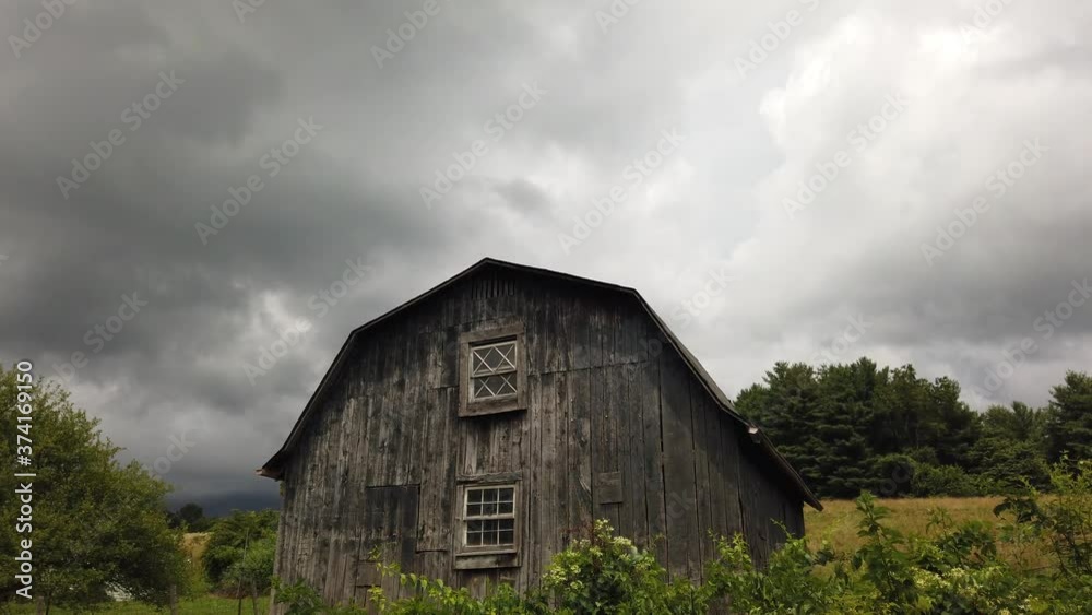 Scenic old rustic farm building in rural countryside farmland by green grass, vegetation and trees, pan up to grey stormy blanket of clouds in cloudy sky, handheld Scenic old rustic farm building in rural countryside farmland by green grass, vegetation and trees, pan up to grey stormy blanket of clouds in cloudy sky, handheld