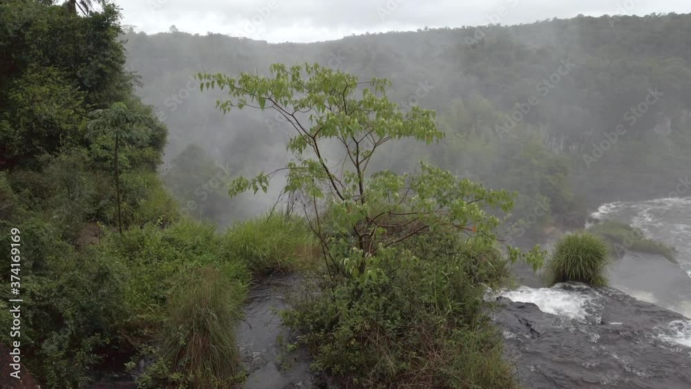 Misty Iguazu falls scene on top of white water flowing and moving down edge of steep mountain cliff to below basin and green vegetation and landscape, handheld close up pan right Misty Iguazu falls scene on top of white water flowing and moving down edge of steep mountain cliff to below basin and green vegetation and landscape, handheld close up pan right