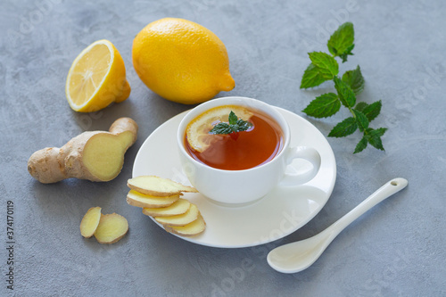 Herbal tea with fresh sliced ginger, lemon and mint on stone background