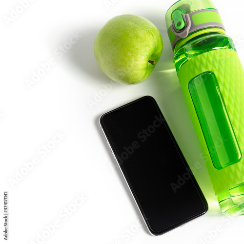 Green fitness bottle. apple and black mobile phone mock up laying near with light leak in the corner. Training application concept. Square format image.