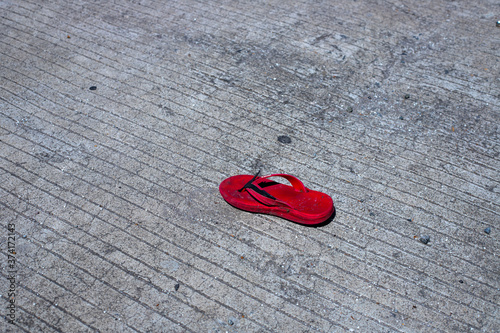 Single red child slipper on asphalt road. Lost kid shoe on street. Safe driving with kids concept. South Asia traffic