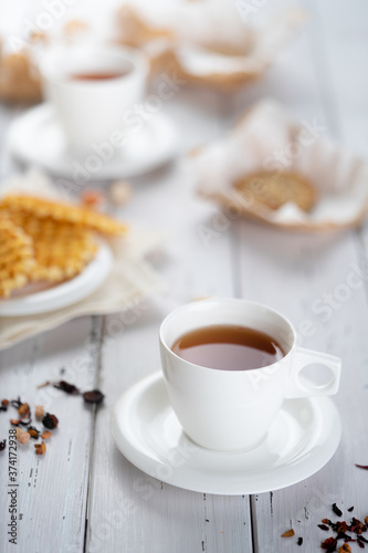 Cup of fresh herbal tea placed on wooden table near snacks for breakfast in morning