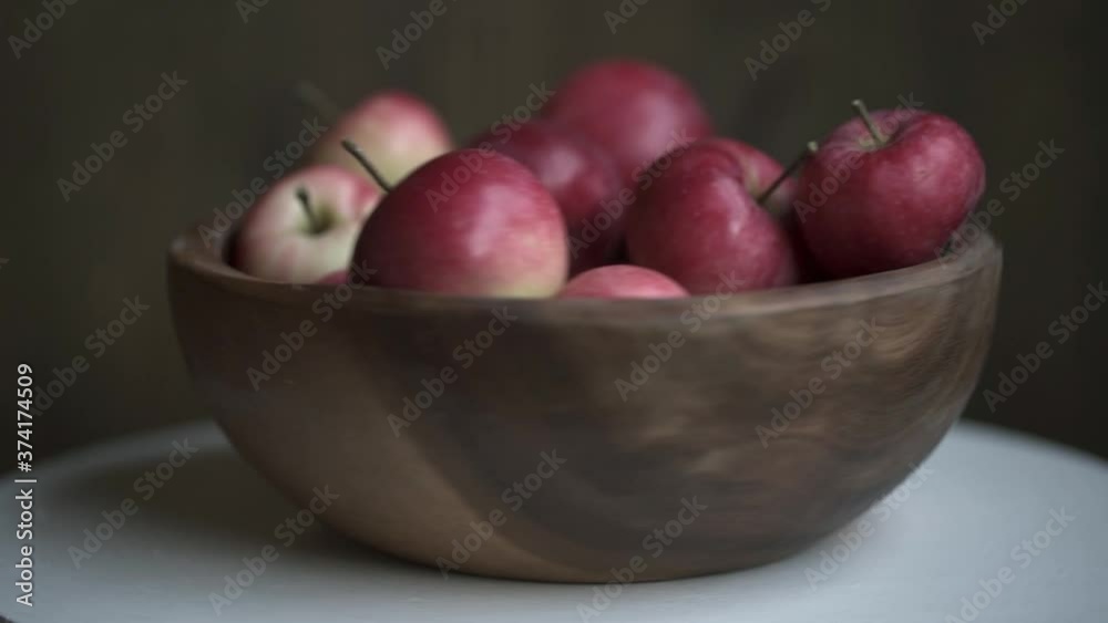 Red apples in wooden bowl rotate on white table. Loopable moving image.